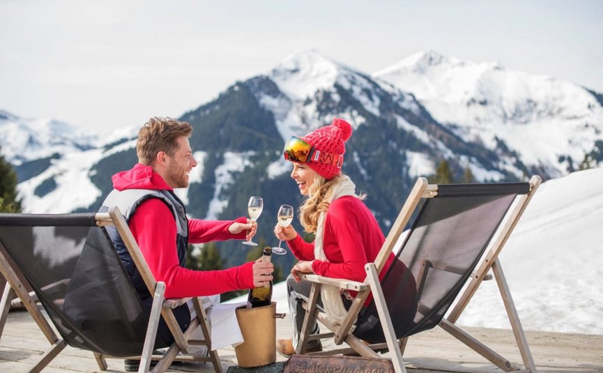 MIDWEEK SPECIAL Couple sitting in snow on deck chairs toasting with champagne glasses