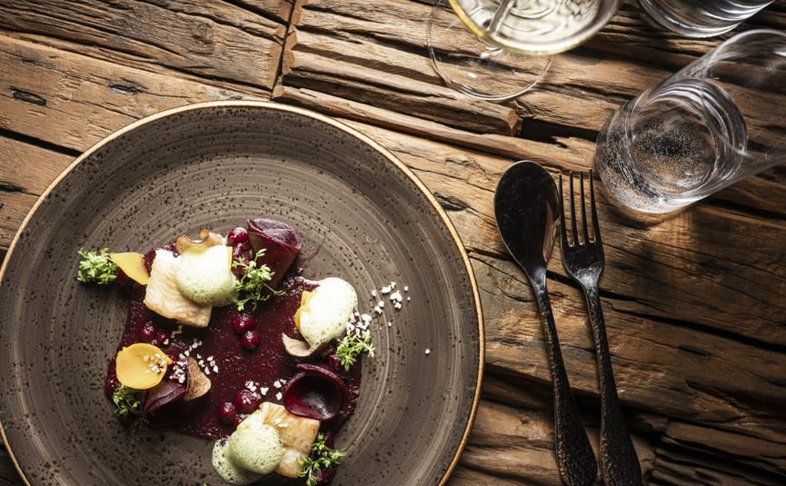 Artistiek gepresenteerd gastronomisch gerecht op rustieke houten tafel met bestek