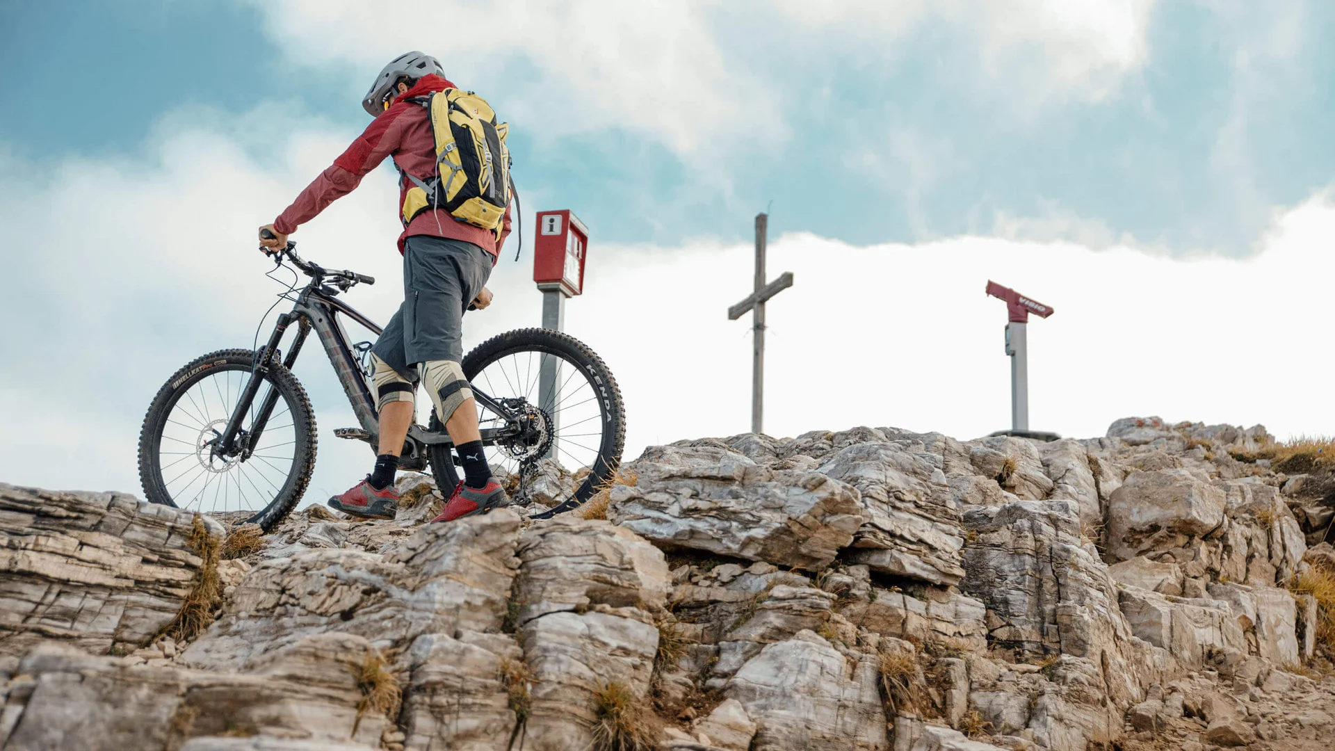 Mountainbiker mit Helm und Rucksack schiebt sein Fahrrad über felsigen Gipfel