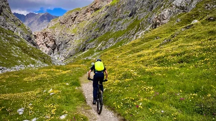 Radfahrer mit grünem Rucksack auf Bergpfad zwischen Felsen und Blumen