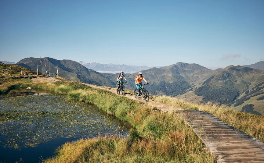 Two mountain bikers riding on a trail with mountains in the background