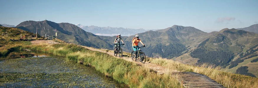 Zwei Mountainbiker auf Bergweg mit Berglandschaft im Hintergrund