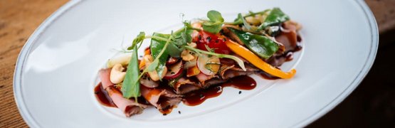 Fein angerichtete Scheiben Fleisch mit Gemüse und Sauce auf weißem Teller