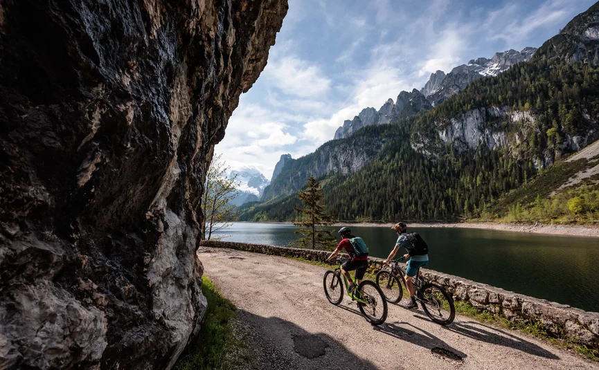 Zwei Fahrradfahrer radeln an einem Bergsee vorbei