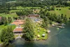 Luftaufnahme eines Ferienresorts am See mit Liegestühlen und Tennisplätzen