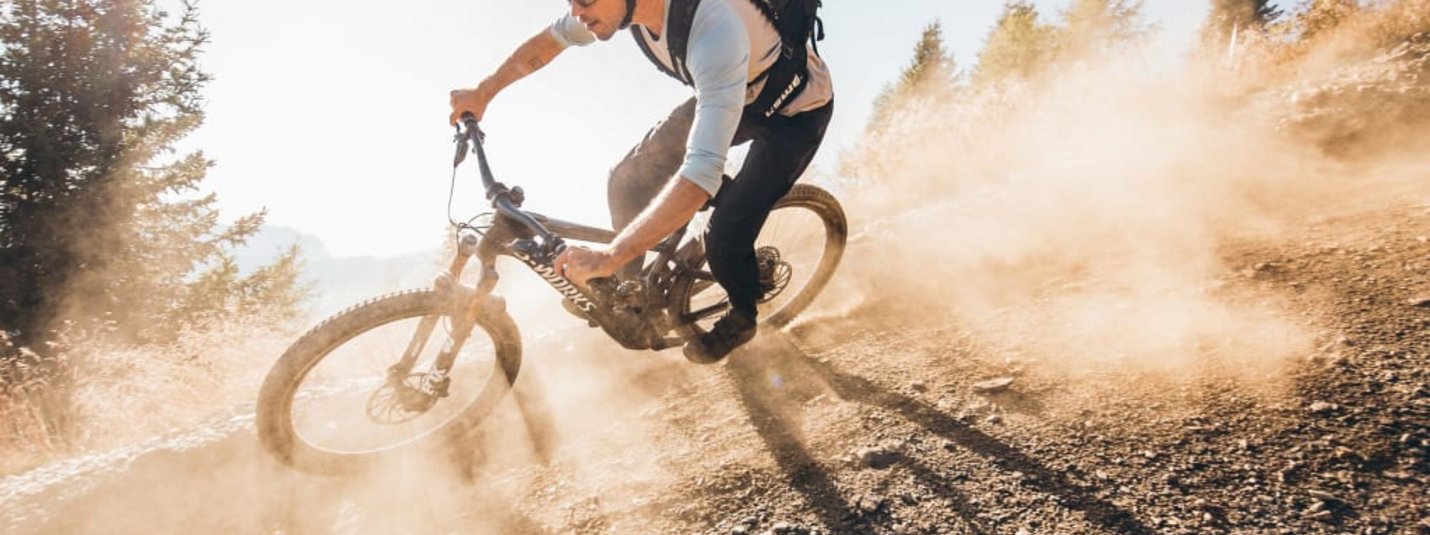 Signature Trail Package Mountainbiker rijdt een stoffige helling af op een zonnige dag