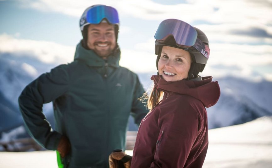 SKI + LOVE Smiling woman and man wearing ski goggles in winter clothing with snowy mountains