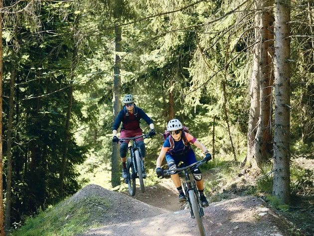 Unterwegs in Österreichs größter Bikeregion © Tobias Köhler Zwei Mountainbiker fahren auf einem Waldweg durch einen sonnigen Wald