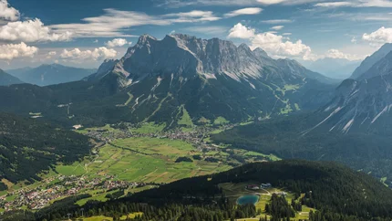 Blick über das grüne Tal mit Bergdorf und gewaltigen Bergen im Hintergrund
