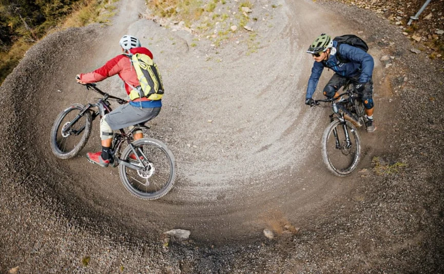 Two mountain bikers riding on a tight, curved gravel trail