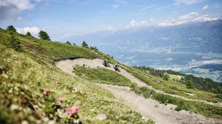 Twee mountainbikers op kronkelig bergpad met uitzicht op de Alpen
