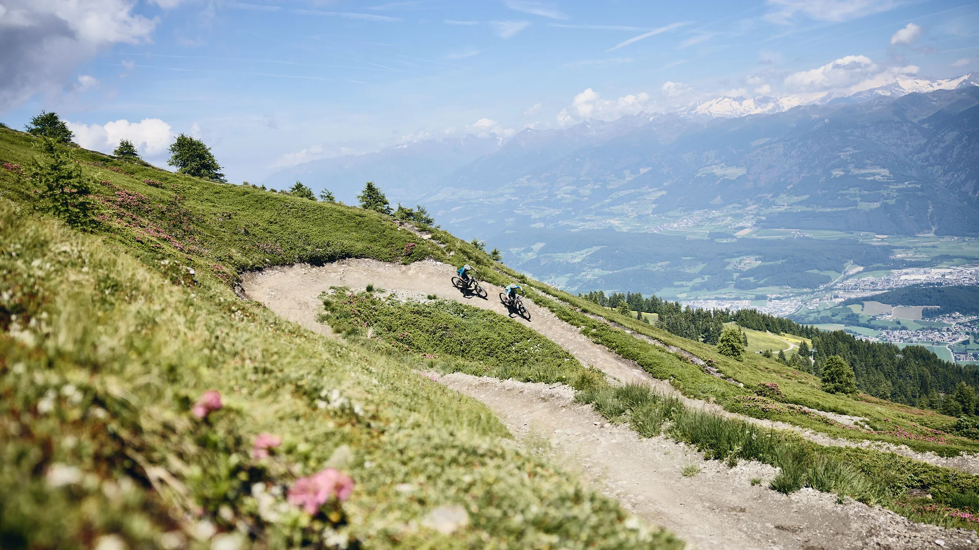 Zwei Mountainbiker auf kurvigen Bergpfad mit Alpenblick