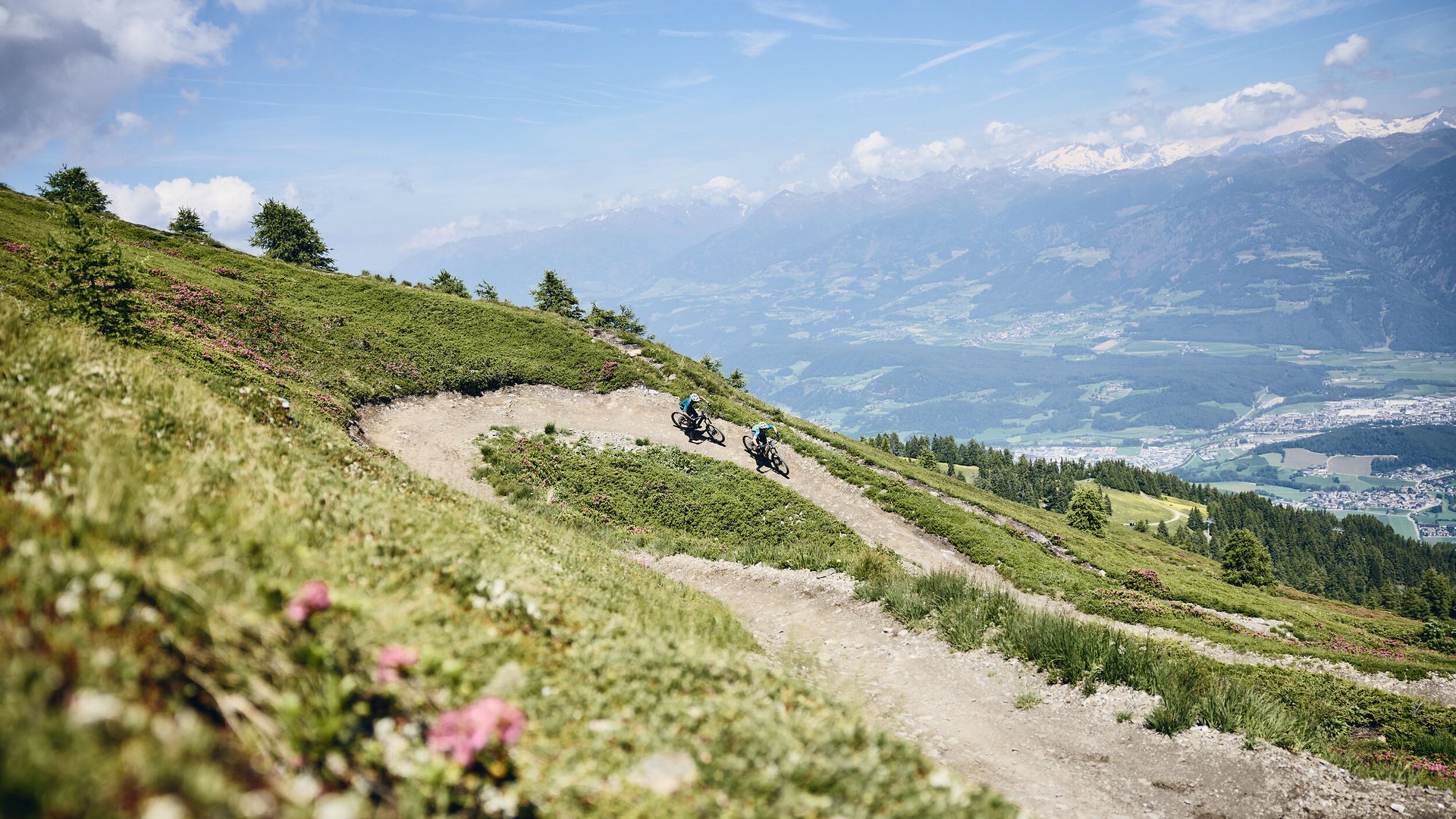 Zwei Mountainbiker auf kurvigen Bergpfad mit Alpenblick
