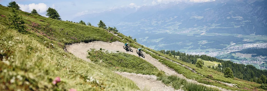 Bruneck - Kronplatz © Tobias Köhler Zwei Mountainbiker auf kurvigen Bergpfad mit Alpenblick