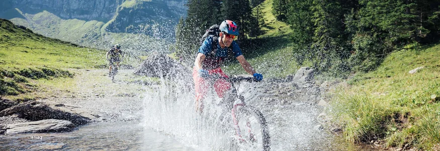 Mountain biker riding through a stream in sunny mountain landscape