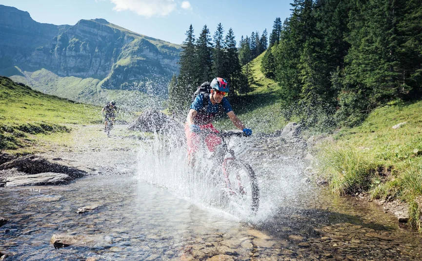 Mountainbiker fährt durch einen Bach in den Bergen bei Sonnenschein