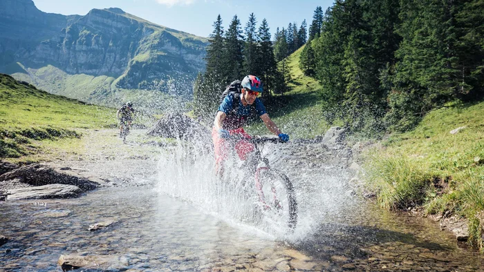 Mountainbiker fährt durch einen Bach in den Bergen bei Sonnenschein