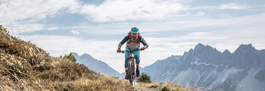 Biken á la Brixen © Dennis Stratmann Fahrradfahrer auf Bergweg mit Bergen und wolkigem Himmel im Hintergrund