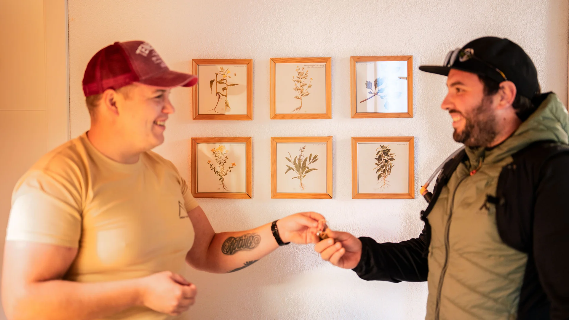 Zwei Männer lächeln und tauschen Schlüssel vor sechs botanischen Bildern an der Wand