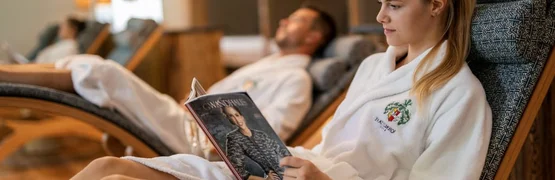 Woman reading magazine in white bathrobe on lounge chair at spa