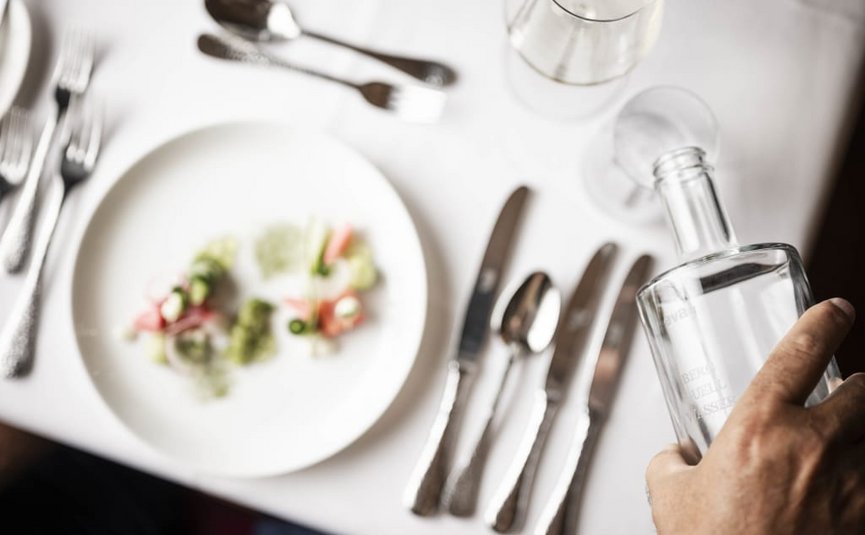 3+1 Short Stay Special Hand hält eine Glasflasche neben einem gedeckten Tisch mit Besteck und Teller