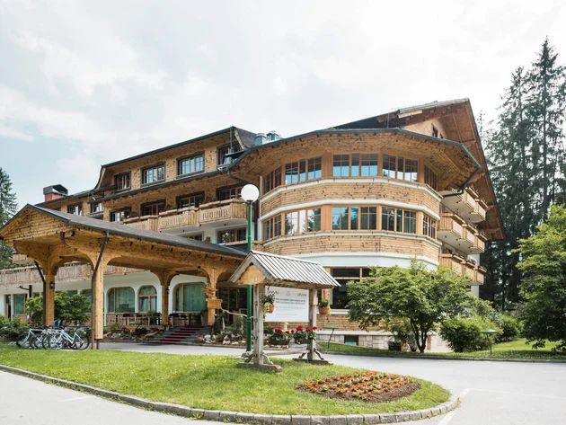 Was steckt hinter dem Umweltengagement von Bikehotels? © Epidos doo Großes Hotelgebäude aus Holz mit überdachtem Eingang und Fahrrädern davor