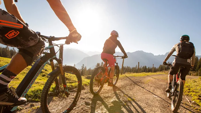 Ein perfekter Enduro-Tag – vom ersten Höhenmeter bis zum letzten Trail © Michael Marte - Bikepark Brandnertal Drei Mountainbiker fahren auf einem sonnigen Bergweg mit Bergen im Hintergrund