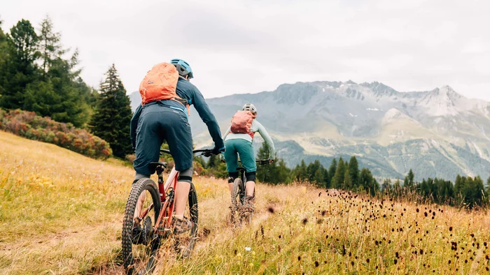 Zwei Mountainbiker fahren auf einem Weg durch ein bergiges Grasland