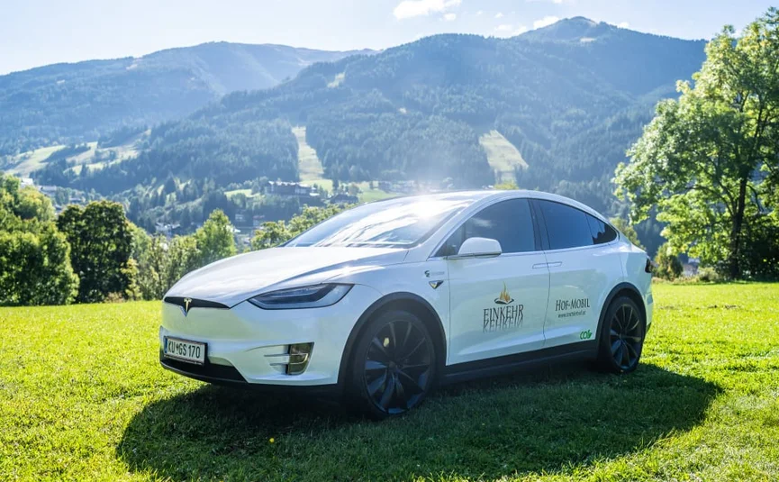 Tesla Nockberge Experience Drive - 3 nights White electric car on green grass with mountains and trees in background