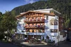 Hotel mit blumengeschmückten Balkonen vor bewaldetem Bergkulisse