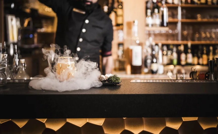 Bartender serving smoky cocktail at bar with bottles in background