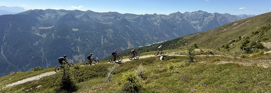 Five mountain bikers on a trail with mountain scenery