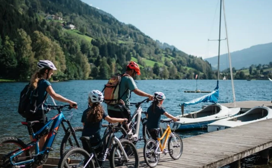 Familie mit Fahrrädern auf einem Steg am See vor Bergen