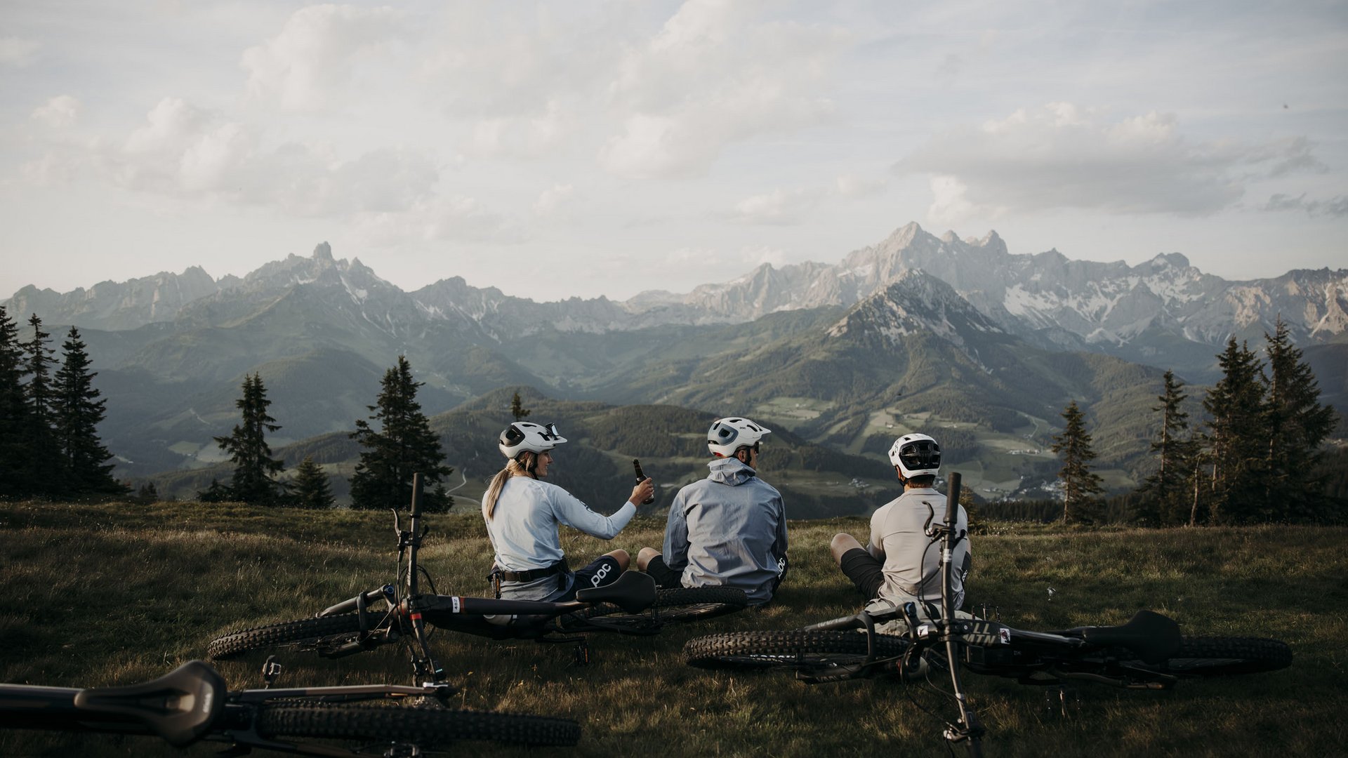 Drei Radfahrer sitzen auf einer Wiese mit Mountainbikes vor Berglandschaft