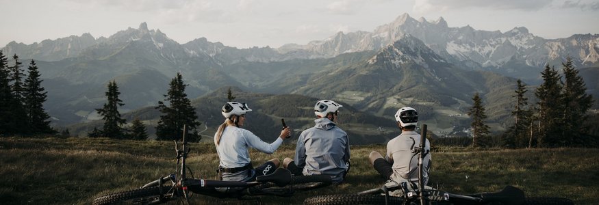 Drie fietsers zitten op gras met mountainbikes voor berglandschap