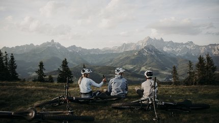Drei Radfahrer sitzen auf einer Wiese mit Mountainbikes vor Berglandschaft