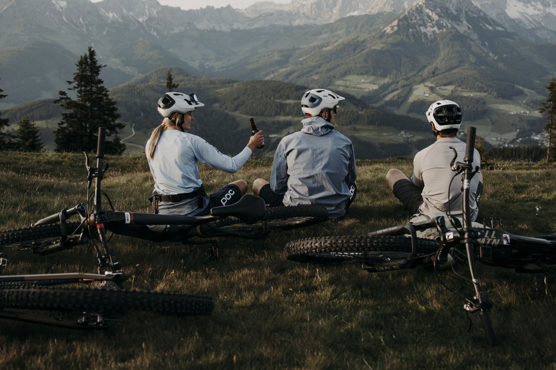 Drei Radfahrer sitzen auf einer Wiese mit Mountainbikes vor Berglandschaft