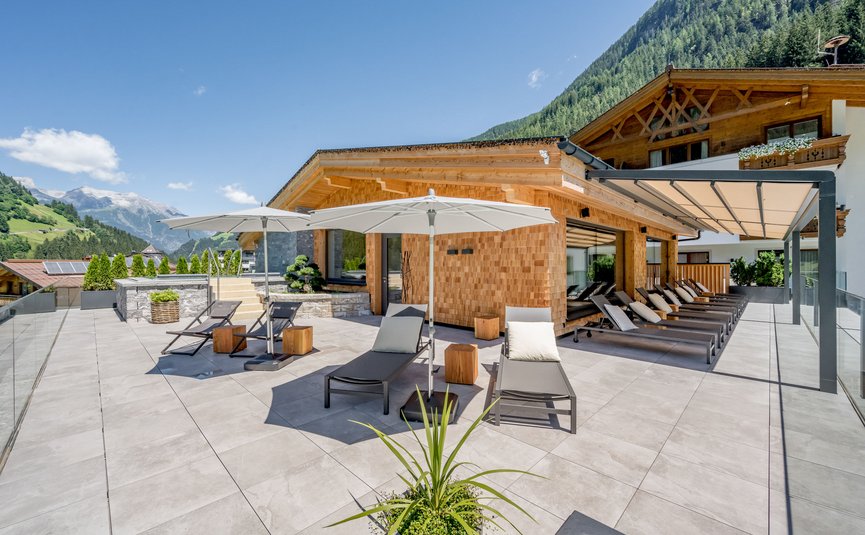 Hotel Weisses Lamm **** © Stephanie Maria Lohmann Terrasse mit Liegestühlen und Sonnenschirmen vor Holzgebäuden in den Bergen