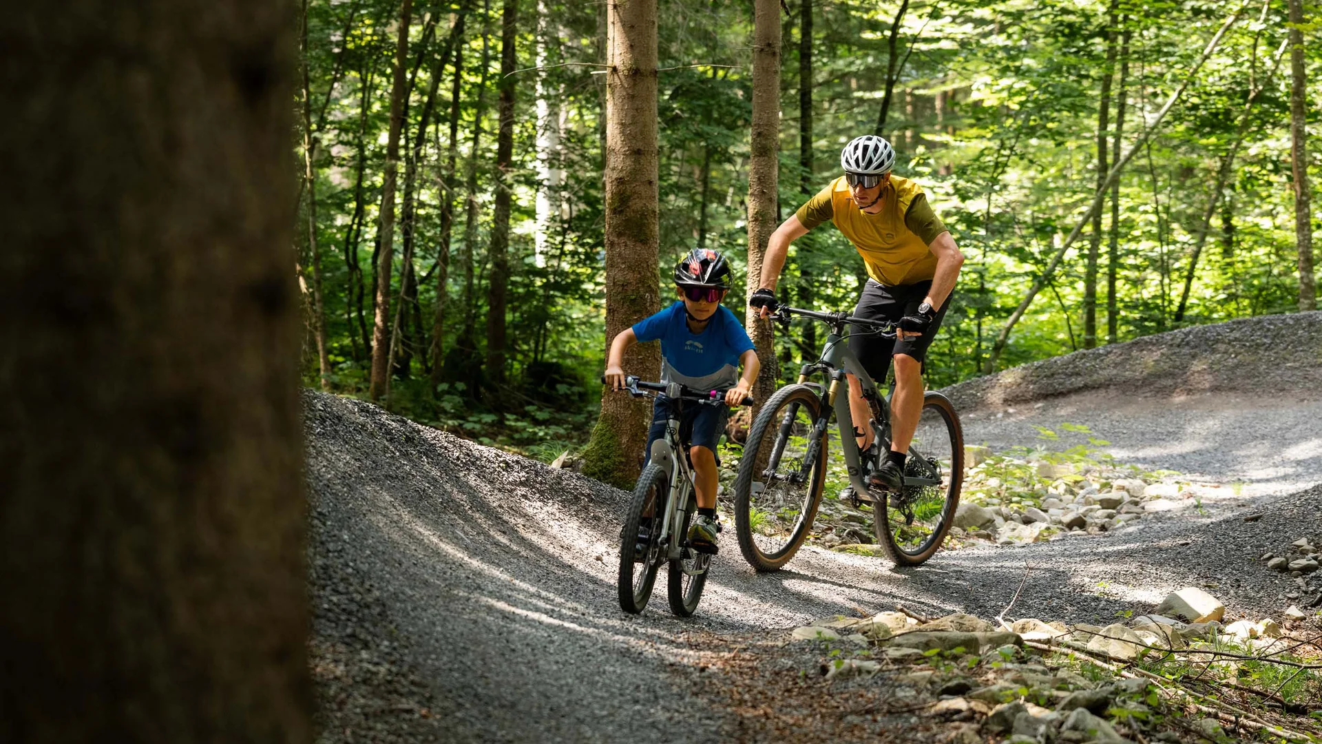 Kind und Erwachsener fahren Mountainbike auf Waldweg