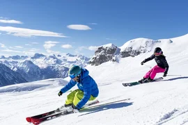 Mid Week 4 Nächte Zwei Skifahrer fahren vor einer schneebedeckten Bergkulisse die Piste hinunter
