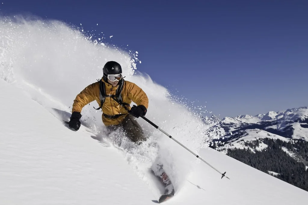 Skiër glijdt door diepe poedersneeuw met bergen op de achtergrond