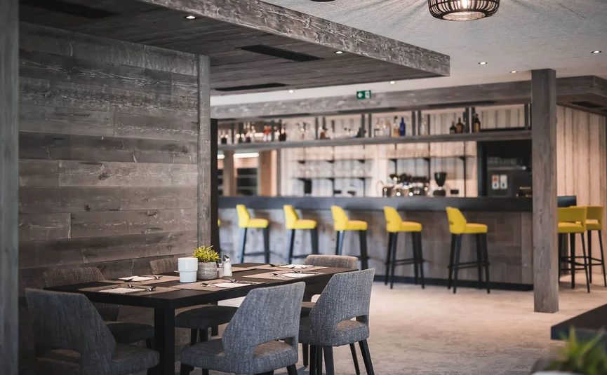 HIRBEN Naturlaub **** © Manuel Kottersteger Modern restaurant with wooden walls, gray chairs, and yellow bar stools