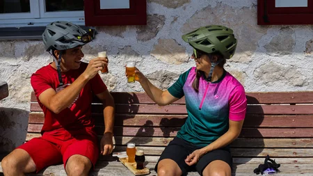 Ein Herbst-Wochenende in San Vigilio © Norman Bielig Zwei Radfahrer stoßen mit Biergläsern auf einer Holzbank an