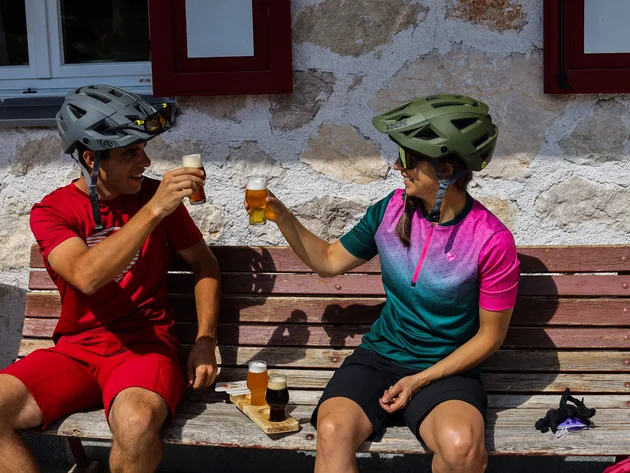 Ein Herbst-Wochenende in San Vigilio © Norman Bielig Zwei Radfahrer stoßen mit Biergläsern auf einer Holzbank an
