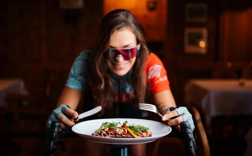 Vrouw in fietskleding met mes en vork voor een bord met eten
