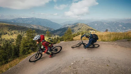 Zwei Mountainbiker fahren auf einem steilen Bergpfad mit Bergen im Hintergrund