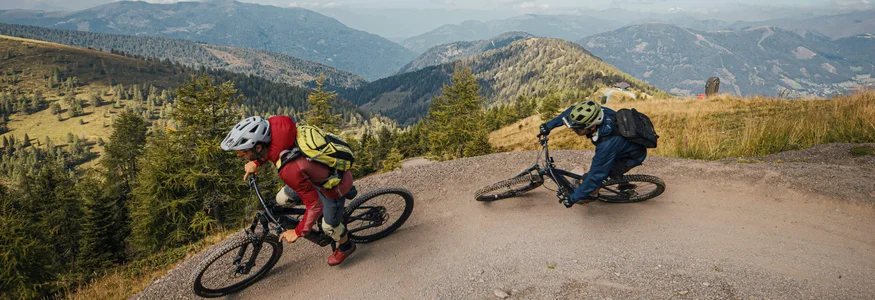 Twee mountainbikers rijden op een steil pad met bergen op de achtergrond