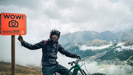 Biker mit Helm neben Fahrrad und Schild mit Foto-Hinweis in den Bergen