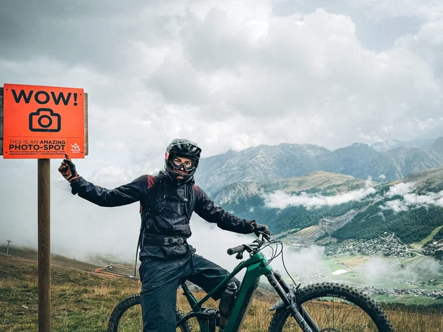 Biker mit Helm neben Fahrrad und Schild mit Foto-Hinweis in den Bergen