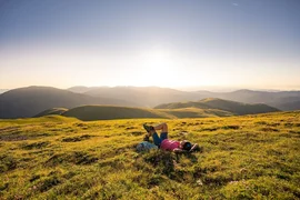 Tesla Nockberge Experience Drive - 3 nights Person relaxing on a green mountain meadow at sunset